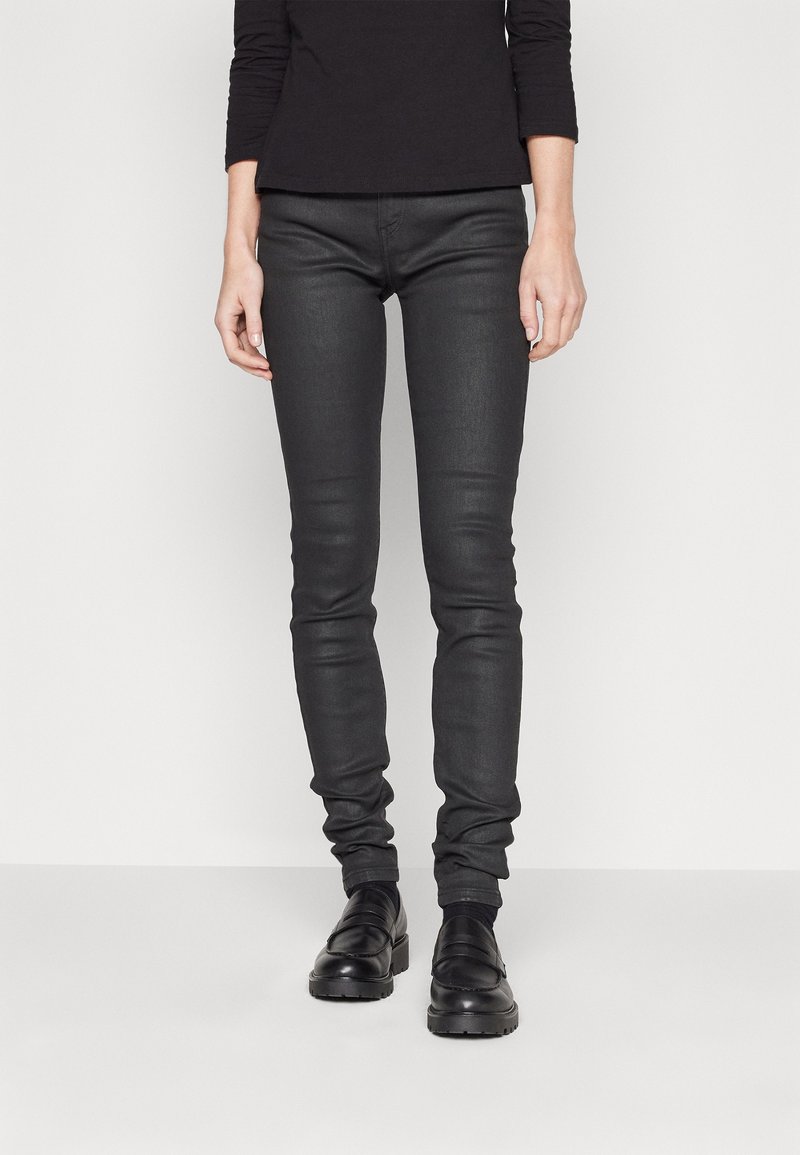 Vaqueros de mezclilla negros ajustados con una textura suave, presentando una cintura de altura media y detalles de costura sutiles, combinados con zapatos negros.