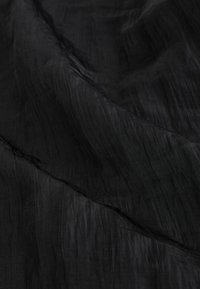 Tissu noir avec une surface texturée, légèrement plissée, mettant en évidence des variations subtiles de brillance et de profondeur. Apparence douce, légère et fluide.