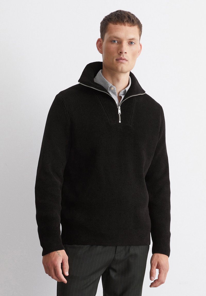 Black corduroy pullover featuring a zip neck, ribbed texture, and a structured design, paired with a collared shirt underneath.