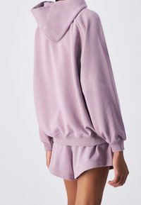 Felpa oversize di colore viola chiaro con cappuccio regolabile. Tessuto morbido e strutturato con polsini elasticizzati, abbinata a pantaloni corti coordinati.