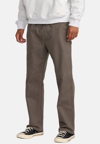 Bruine rechte broek met zichtbare stiksels, gemaakt van duurzaam materiaal. Gekocht met een grijze sweatshirt en zwarte sneakers.