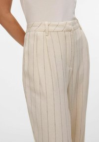 Beige gestreepte broek van textuurstof, met plooien, een tailleband en een zijzak. Verticale strepen in donkere tinten.