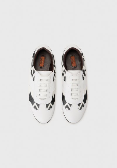 Λευκά αθλητικά παπούτσια με μαύρο ζιγκ-ζαγκ σχέδιο, δερμάτινο επάνω μέρος, επίπεδες κορδόνια και καφέ υπόστρωμα με το όνομα της μάρκας. Ελαστική σόλα.