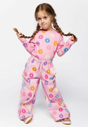 Ružový loungewear set vyrobený z bavlny, ktorý obsahuje top s dlhými rukávmi a voľné nohavice, oboje s farebnými vzormi jabĺk rôznych odtieňov.