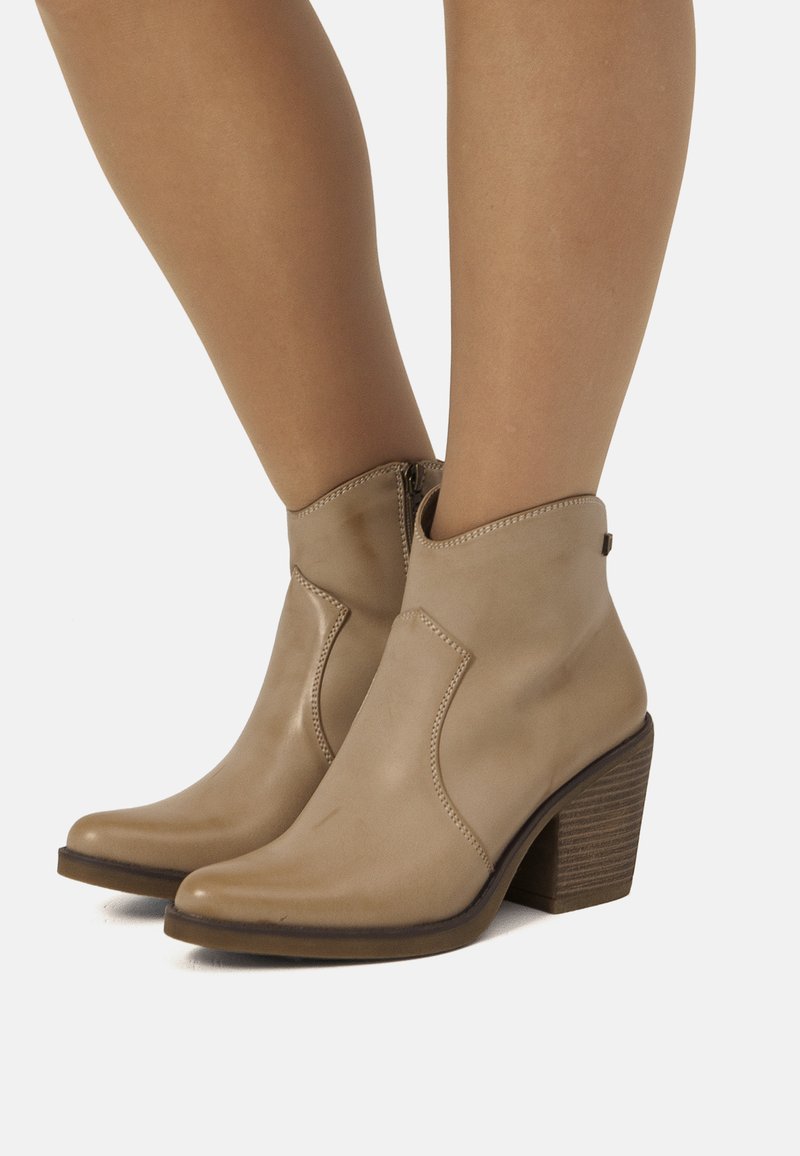 Botines de cuero beige hasta el tobillo con puntera puntiaguda, cremallera lateral y un tacón de madera apilada. Costuras decorativas a lo largo de las costuras.