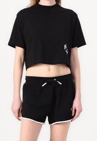 Svart kortärmad t-shirt i mjukt tyg, med korta ärmar och en liten logotyp. Matchas med svarta shorts med vit kant och dragsko.