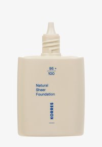 Beige rechteckige Flasche mit einer spitzen Kappe, die mit "95+ / 100 Natürliche transparente Foundation" beschriftet ist, und dem Markennamen "KORRES" in blauer Schrift.