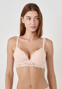 Reggiseno in pizzo rosa chiaro con motivo floreale, coppe con ferretto, spalline regolabili e bordi ondulati. Texture morbida e dettagli delicati.