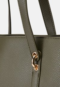 Olīvu zaļas ādas somiņa ar teksturētu apdari, ar gludām rokturiem un zelta tonī metāla gredzenu piestiprināšanai.