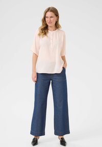 Bluză roz deschis cu decolteu henley și mâneci scurte, asortată cu pantaloni din denim largi de culoare albastru închis. Design minimalist, textură netedă.