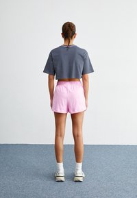 Grå kortärmad t-shirt och ljusrosa shorts. Materialet verkar mjukt med ett elastiskt midjeband på shortsen. Sneakers synliga på fötterna.