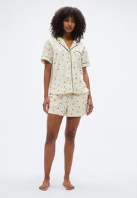 Σετ πυτζάμες ανοιχτού χρώματος με κοντά μανίκια και σορτς, με μαύρα λουλουδάτα σχέδια και πράσινη επένδυση κατά μήκος του γιακά και των μανικιών.