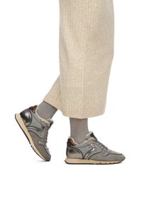 Graue Sneaker mit einer Mischung aus Wildleder und metallischen Akzenten, ausgestattet mit einem flauschigen Kragen, Schnürsenkeln und einer weichen Gummi-Sohle, kombiniert mit cremefarbenen, gerippten Hosen.