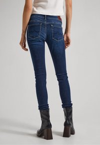 Slim jeans i mörkblå denim, med två bakfickor med ett vågmönster. Matchat med svarta klackboots som går till anklarna.