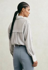 Triibuline nööpidega särk pika varrukaga, valge ja mereväe sinise tooniga, sobitatud kohandatud helesiniste pükstega, millel on tagataskud.