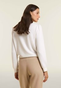 Suéter blanco texturizado con mangas abullonadas, combinado con pantalones beige suaves. El suéter presenta un diseño simple y moderno con puños en las muñecas.