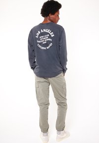 T-paita pitkällä hihalla, tummansininen, valkoisella painatuksella takana. Yhdistetty vaaleanharmaisiin cargo-housuihin, joissa on sivutaskut ja joustavat hihansuut.