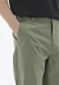 Pantaloni ușori de culoare verde măslin, cu o textură netedă. Caracteristici includ buzunare laterale și un design subtil, simplificat.