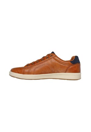 Zapatilla de cuero marrón con perfil bajo, suela de goma crema y acentos de tela azul oscuro en el talón. Presenta seis ojales de bronce y detalles de costura.