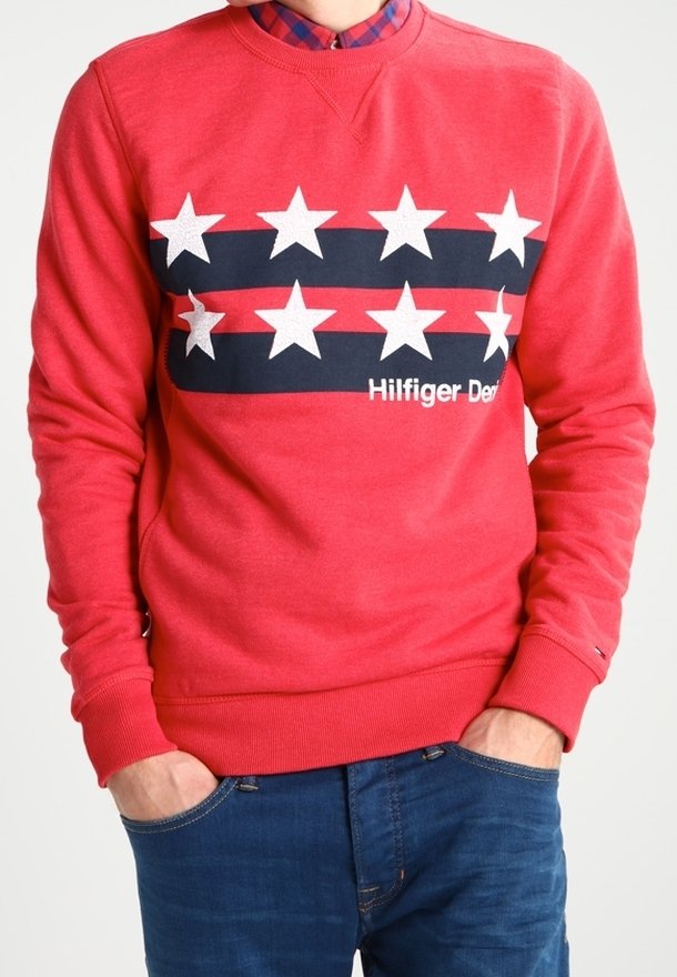 Sudadera roja con cuello redondo, mangas largas y un diseño frontal de estrellas alternas en negro y blanco, con el texto "Hilfiger Denim".