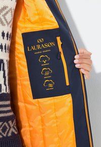 Námořnická bunda s oranžovým podšíváním; obsahuje štítky o voděodolnosti, prodyšnosti a větruodolnosti. Kapsa se zipem na vnitřní levé straně.