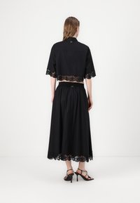 Svart crop top og lang skjørt-sett, begge med blonder på kantene. Toppen har korte ermer og krage, mens skjørtet har elastisk midje.