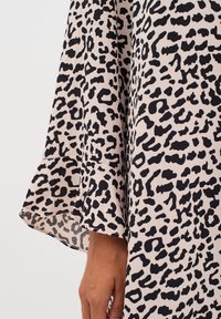 Kleid mit Glockenärmeln aus weichem Stoff, das einen beigen Hintergrund mit auffälligem schwarzem Tiermuster und einer fließenden Silhouette aufweist.