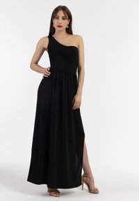 Rochie maxi neagră cu un singur umăr, cu un corset ajustat, talie strânsă și fanta pe lateral. Material neted cu o siluetă fluidă, asortată cu pantofi cu toc bej.