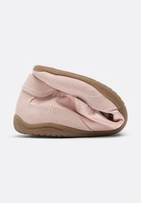 Chaussure en daim rose doux pliée en deux, montrant une semelle flexible marron texturée et une tige cousue, isolée sur un fond clair.