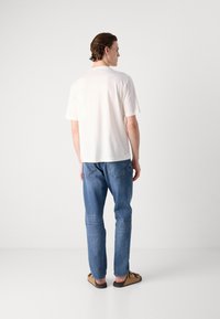 Hvit bomulls T-skjorte med korte ermer, løs passform. Kombinert med blå denimjeans og brune sandaler. Enkel design uten synlige detaljer.