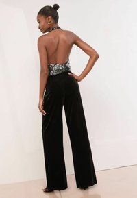 Pantaloni largi din catifea neagră asociați cu un top halter cu paiete. Topul are un design cu spate decupat, adăugând contrast texturii lucioase.