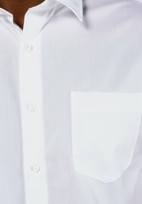 Weißes Button-up-Hemd aus leichtem Stoff, mit einer linken Brusttasche und subtiler Textur mit Stickerei-Details auf der Tasche.