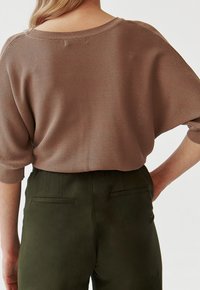 Przytulny, brązowy sweter w dużym rozmiarze z szerokim dekoltem i krótkimi rękawami, zestawiony z ciemnozielonymi spodniami o wysokim stanie z kieszeniami w szwach.