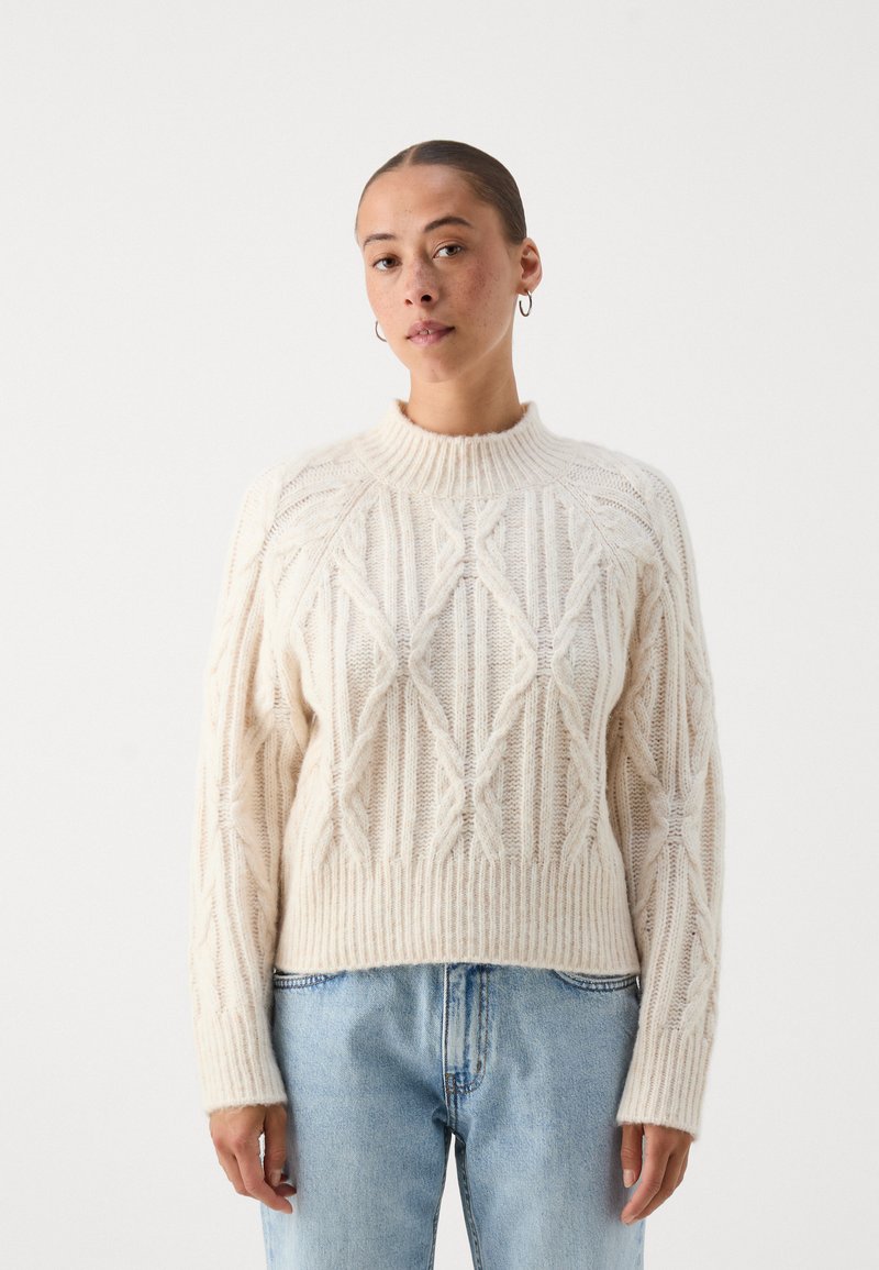 Πλεκτό πουλόβερ σε κρέμ απόχρωση με υφή διαμαντιών, ριμπ λαιμόκοψη και στρίφωμα, σε συνδυασμό με ανοιχτό μπλε τζιν. Χαλαρή εφαρμογή, μακριά μανίκια.