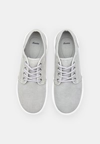 Sneaker in tela grigia con suole in gomma bianca, caratterizzate da punta arrotondata, design con lacci e una texture sottile. Logo visibile sulla fodera interna.