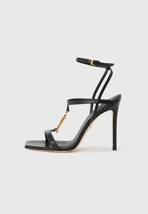 Black high-heeled sandal with thin straps, gold hardware detail, open toe design, and a smooth leather texture. Features a slender stiletto heel.