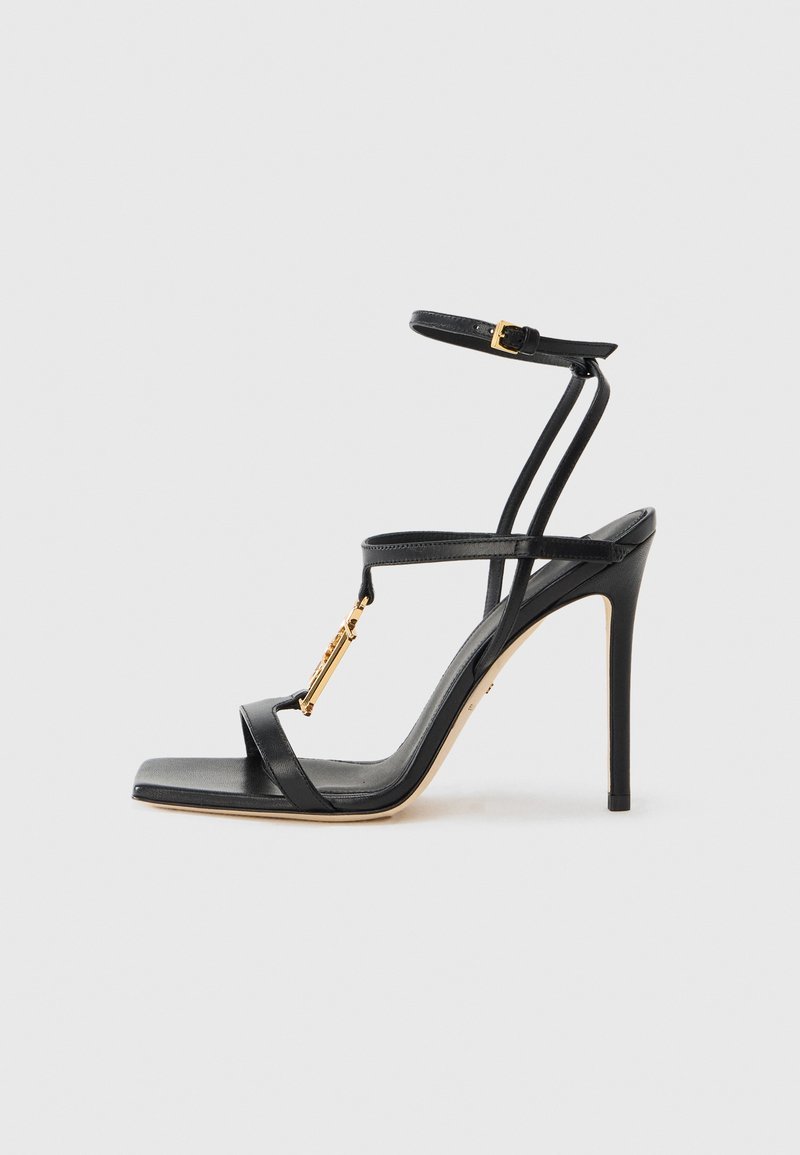 Black high-heeled sandal with thin straps, gold hardware detail, open toe design, and a smooth leather texture. Features a slender stiletto heel.
