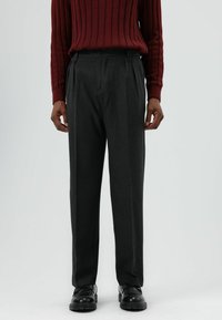 Grijze op maat gemaakte broek met een rechte pijp, plooien aan de voorkant, gemaakt van een gestructureerde stof, gecombineerd met zwarte schoenen.