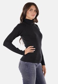 Maglione nero a collo alto con maniche lunghe, design aderente, polsini e orlo a costine. Texture in maglia, tessuto liscio e silhouette aderente.
