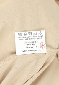 Beige cotton T-shirt with care label. Smooth texture, stitched hem, features washing instructions, and made in Bangladesh.