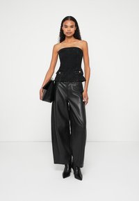 Zwarte strapless denim korset top met gouden knoopaccenten, gecombineerd met brede zwarte leren broeken en strakke zwarte enkellaarsjes.