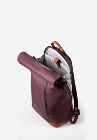 Bordeauxfarbener Rolltop-Rucksack aus strapazierfähigem Material mit einem Basis aus hellbraunem Leder. Verfügt über eine Reißverschlusstasche und ein graues Innenfutter mit Fächern.