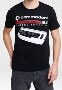 Osoba w czarnym podkoszulku z grafiką komputera Commodore 64 i napisem "komputer do gier commodore 64."