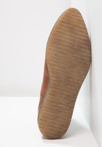 Brown leather shoe sole with a textured, ridged pattern. The heel is tapered and the edge features a smooth finish.