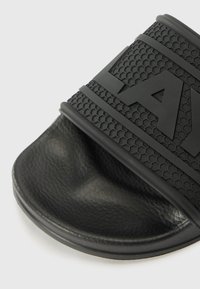 Black slide sandal with textured upper featuring hexagonal pattern and branding. Made of rubber with a smooth footbed and rounded edge.