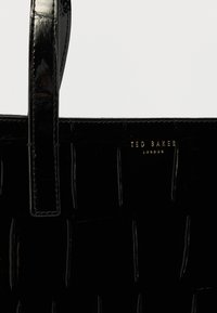 Czarna torba typu tote z lakierowanej skóry o plecionej fakturze, z krótkimi uchwytami i złotym logo "TED BAKER LONDON" na przodzie.