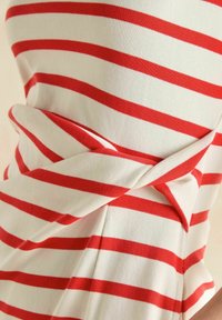 Rot-weiße gestreifte Bluse aus weichem, elastischem Material. Besitzt ein verdrehtes Design an der Taille, das einen drapierten Effekt erzeugt.