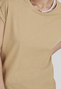 Beige bomull t-shirt med korta ärmar, rundad halsringning och mjuk textur. Har en subtil glans och inga märkbara mönster eller grafik.
