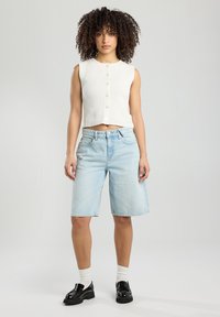 Valkoinen ribattua kangasta crop-top, jossa on napit, yhdistettynä vaaleansinisiin farkkushortseihin. Mallilla on päällään mustat kengät ja valkoiset sukat. Yksinkertainen, rento ilme.