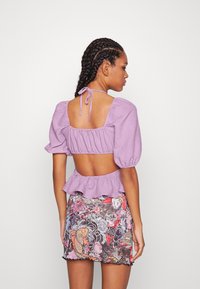 Blusa lilás de mangas bufantes com costas abertas, combinada com uma saia mini de padrão floral com desenhos de carpas e flores. Tecido texturizado.